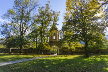 Manglisi Sioni Katedrali. Avluya kemerli girişi olan çan kulesi. Taş kale duvarı. Ağaçlar, çimenler