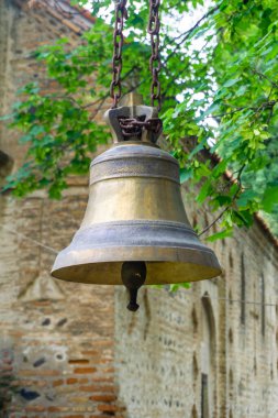 An old ornamented bronze bell hangs on a rusty chain near a church clipart