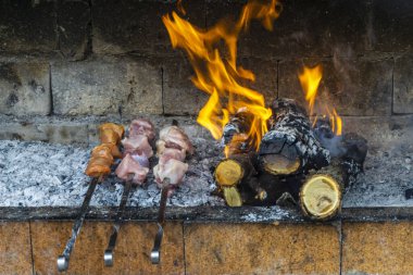 Yanan dalların yanındaki tuğla fırında et kızartıyorlar. Ateşin kömürü ve alevleri görünür