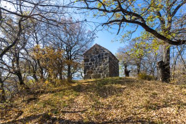 Tepedeki sonbahar ağaçlarının arasındaki taş bazilika. Sonbahar renkleri. Bulutlu mavi gökyüzü