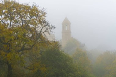 Church of St. Ekvtime in Kiketi village on a foggy morning. Trees with autumn leaves, bushes in the foreground clipart