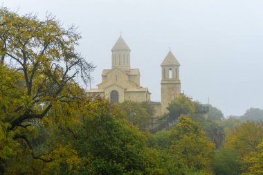 Sisli bir sabahta St. Ekvtime Kilisesi ve Kiketi köyündeki çan kulesi. Sonbahar yapraklı ağaçlar, ön planda çalılar.