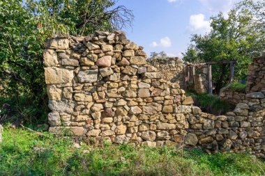 Güneş ışığıyla aydınlatılmış büyük taşlardan yapılmış eski bir harabe duvar. Çimenler ve ağaçlar