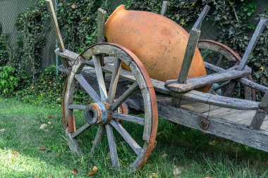 Clay Qvevri, büyük tekerlekli ahşap bir arabada büyük bir kil sürahi. Paslı jantlar, yeşil çimenler, yapraklar