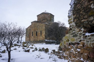 Jvari Monastery in snowy cloudy weather. Falling snow and snow covered fields are visible clipart