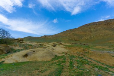 Genç yeşil çimenler kumtaşı kayaları üzerinde. Arka planda bulutlar ve kayalar olan mavi gökyüzü
