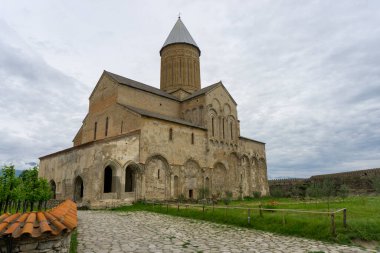 Alaetti Manastırı 'nın Aziz George kilisesinin olduğu avlu. Yeşil tarla, taş çit, üzüm bağı. Bulutlu gökyüzü