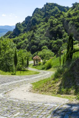 The paved road of the Shio-Mgvime monastery descends down to the foot of the mountain. Hills with trees, bright blue sky in the background clipart