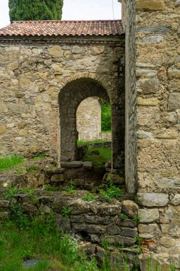 Ikalto Akademisi 'nin ana kilisesinin kemerli girişinin yan görüntüsü. Taş duvarlar, yeşil çimenler.