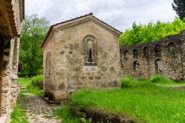 Ikalto Akademisi 'nin bahçesinde küçük bir kilise. Taş duvarlar, kemerli bir pencere. Yeşil çimenler, bulutlu bir gökyüzü.