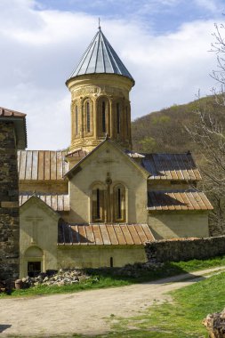 Kvatakhevi manastırının avlusundaki kilise. Taş duvarlar, fayanslı çatı. Taş yollar, yeşil çimenler, parlak mavi gökyüzü..