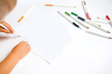 Çocukların elleri beyaz kağıda renkli kalemler çiziyor.