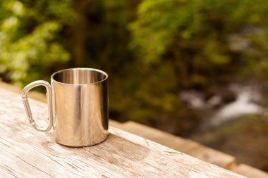 Ormandaki ahşap masada su olan boş metal bardak, metin için yer.