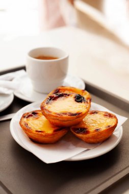 Bir tabak sade kahveyle geleneksel Portekiz Pastel de Nata tabağına yakın çekim. Kırsal masada çıtır kremalı tart ve espresso. Kahvaltı ya da tatlı için mükemmel.
