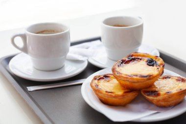 Bir tabak sade kahveyle geleneksel Portekiz Pastel de Nata tabağına yakın çekim. Kırsal masada çıtır kremalı tart ve espresso. Kahvaltı ya da tatlı için mükemmel.
