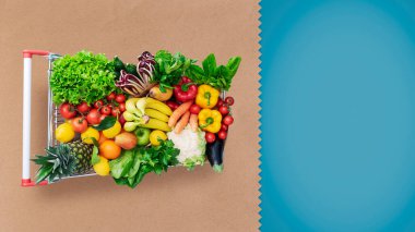 Supermarket shopping cart full of fresh vegetables and fruits, copy space clipart