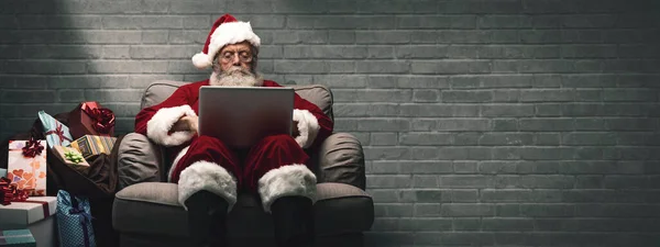 サンタ クロース家でのんびりと彼がチャット ノート パソコンとの接続とソーシャルネットワー キング クリスマスの時間と技術の概念 — ストック写真