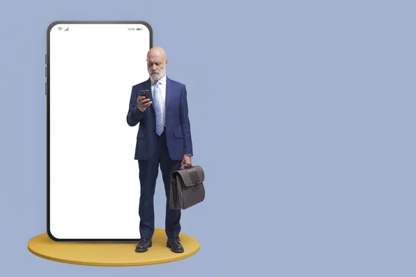 企业商人站在一个屏幕空白的大型智能手机旁边 他正在检查自己的手机 — 图库照片