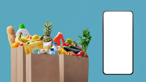 Full grocery bags and smartphone with blank screen, online grocery shopping app concept