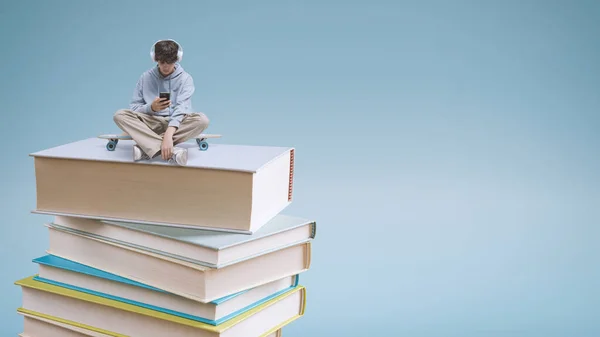 Young school student using a smartphone and sitting on a pile of books: online learning and education concept