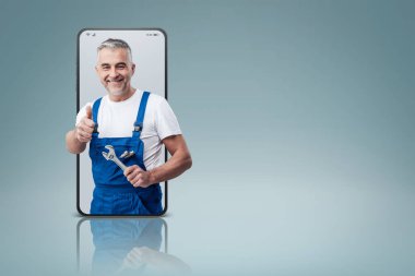 Cheerful repairman and plumber giving a thumbs up in a smartphone videocall and smiling, online  service concept