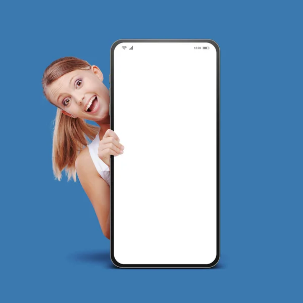 快乐的年轻女性微笑着 在有空白屏幕的大型智能手机后面窥视着 — 图库照片