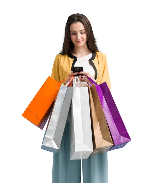 彼女のスマートフォン上のショッピングアプリを使用して オンラインショッピングを行う幸せな若い女性は 彼女はカラフルなショッピングバッグの多くを運んでいます — ストック写真
