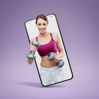 Smiling young sportswoman working out with dumbbells in a smartphone videocall and smiling, online  service concept