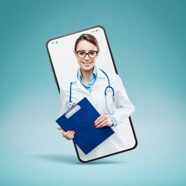自信を持って若い女性医師の笑顔とスマートフォンのビデオコールと笑顔でクリップボードでポーズ オンラインサービスの概念 — ストック写真