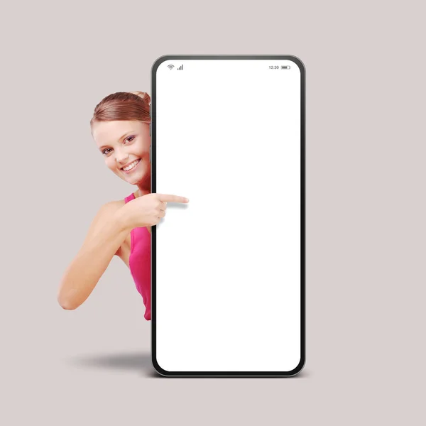 快乐的年轻女人笑着 展示着一部大智能手机 指着空白的屏幕 — 图库照片
