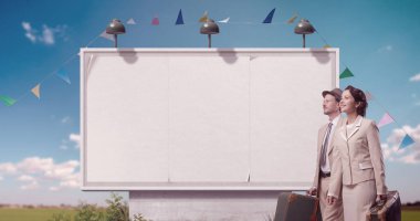 Arka planda bavul tutan ve gezen, boş büyük reklam panosu olan mutlu klasik tarz bir çift.