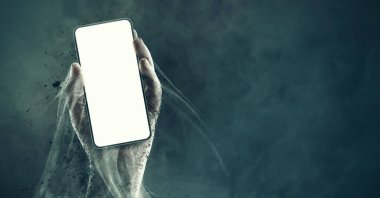 Korku ve Cadılar Bayramı konseptiyle akıllı telefonu tutan ürkütücü zombi el.