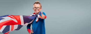 Smiling cute superhero thumbs up, he is wearing a British flag as a cape