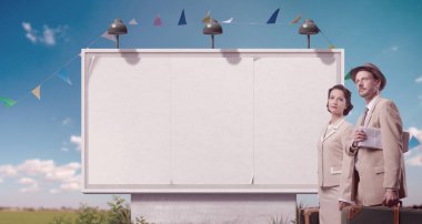 Arka planda bavul tutan ve gezen, boş büyük reklam panosu olan mutlu klasik tarz bir çift.