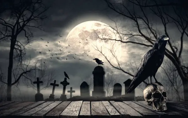 Creepy old cemetery at night with spooky crow standing on a human skull, full moon in the background: horror and Halloween concept