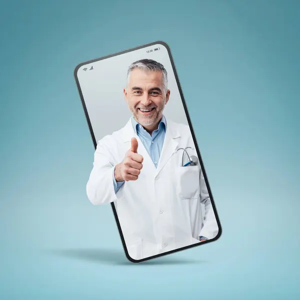 stock image Professional doctor giving a thumbs up in a smartphone videocall and smiling, online doctor and telemedicine service concept