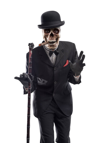 Evil elegant Halloween character with skull head posing and looking at camera, he is wearing a suit and a bowler hat