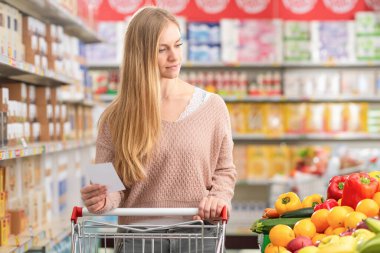 Çekici genç bir kadın alışveriş arabasını itiyor ve marketten alışveriş yapıyor.