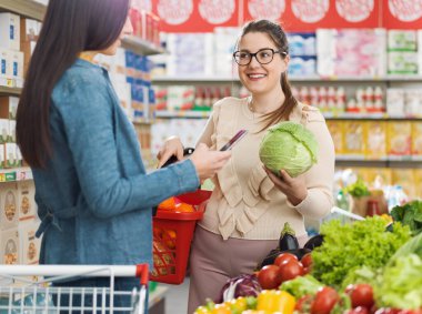 Süpermarkette buluşan mutlu kadınlar, konuşuyorlar ve birlikte sağlıklı sebzeler alıyorlar, market alışverişi ve yaşam tarzı konsepti.