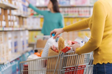 Marketteki kadın, bir alışveriş arabası itiyor ve ürünler alıyor.