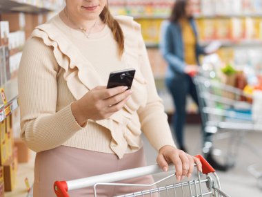 Müşteri süpermarkette alışveriş yapıyor ve akıllı telefonunu kullanıyor.