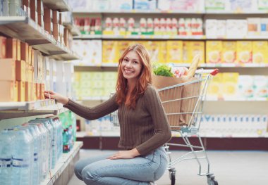 Süpermarketteki genç bir kadının portresi. Raftan ürünleri alıyor ve kameraya gülümsüyor.