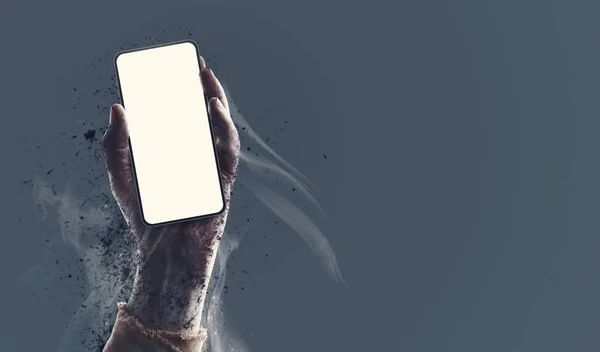 Creepy zombie hand holding a smartphone with blank screen, horror and Halloween concept