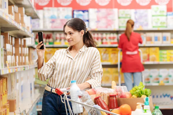 Woman doing grocery shopping at the supermarket, she is checking product information using a scanner app on her smartphone