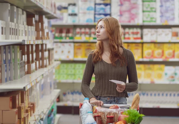 Jovem Fazendo Compras Supermercado Ela Está Empurrando Carrinho Completo Segurando — Fotografia de Stock