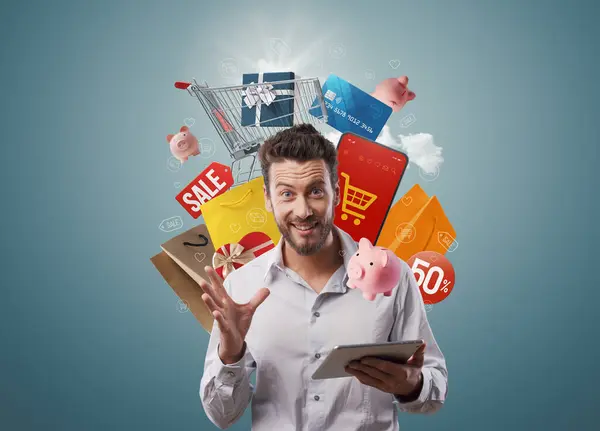 Excited happy man holding a tablet and doing online shopping, he is surrounded by shopping items, offers and sale concept