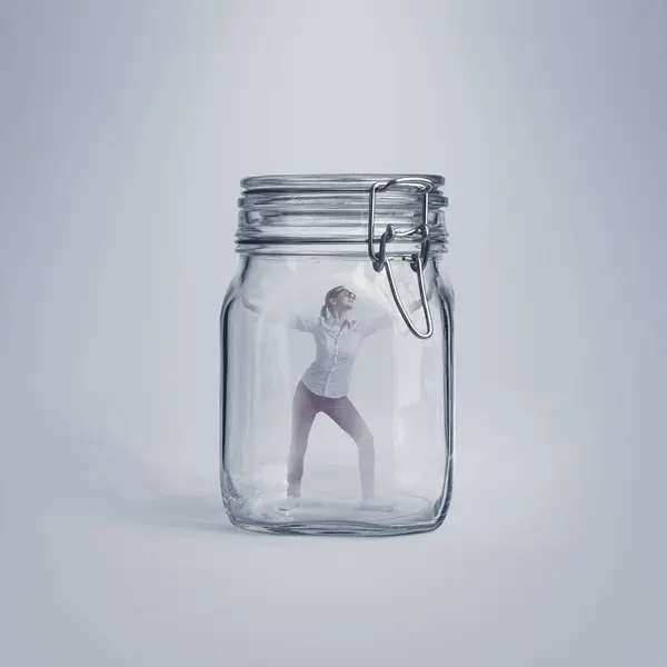 Scared young woman trapped in a huge glass jar, she is desperate and unable to escape
