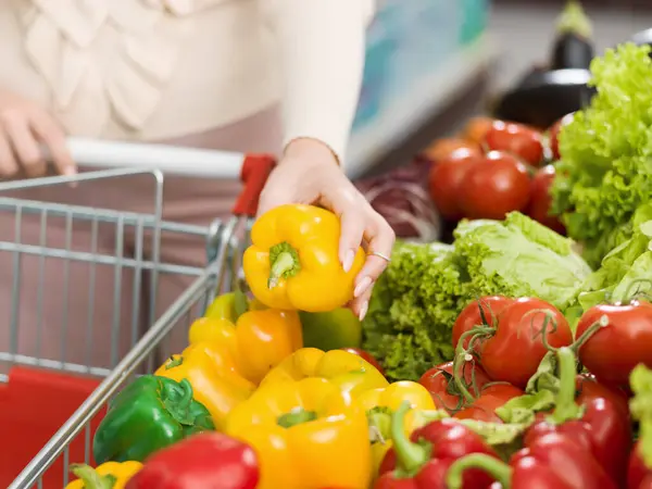 トロリーを押し スーパーマーケットで新鮮な野菜を買う女性 彼女はベルペッパーを選んでいます — ストック写真