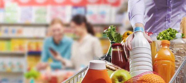 Woman putting fresh groceries in the shopping cart at the grocery store, grocery shopping and retail concept, copy space