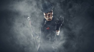 Şık bir takım elbise giymiş korkunç, şeytani bir karakter. Kameraya bakıyor ve etrafı sis ve korku ile çevrili bir şekilde duruyor.